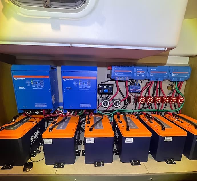 Six SOK batteries bracketed to the floor of a boat locker, wired to two Victron Quattro inverters, a Cerbo GX and fused DC distribution