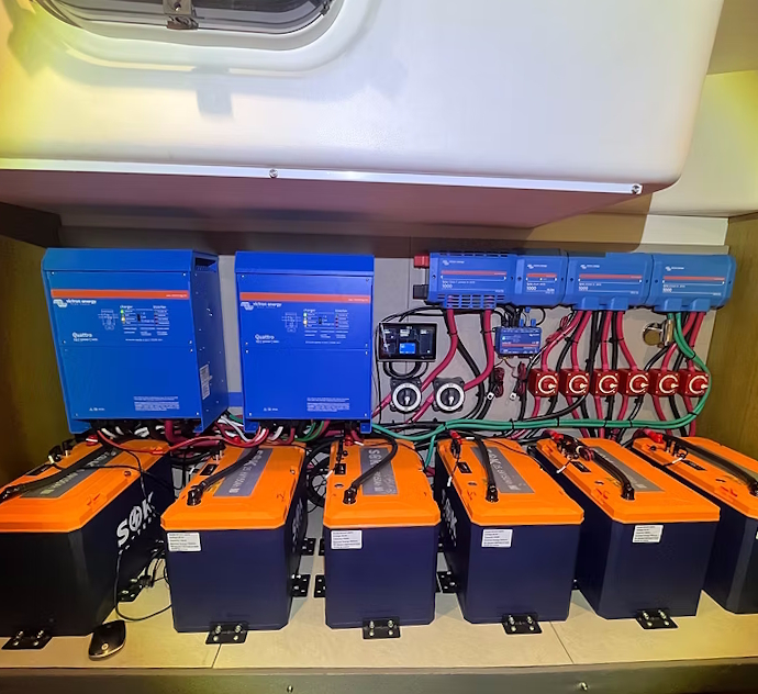 Six SOK batteries bracketed to the floor of a boat locker, wired to two Victron Quattro inverters, a Cerbo GX and fused DC distribution